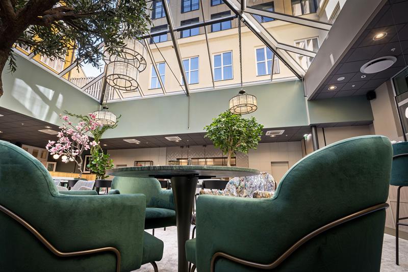 Restaurantinteriør med glasstak og grønne lenestoler.