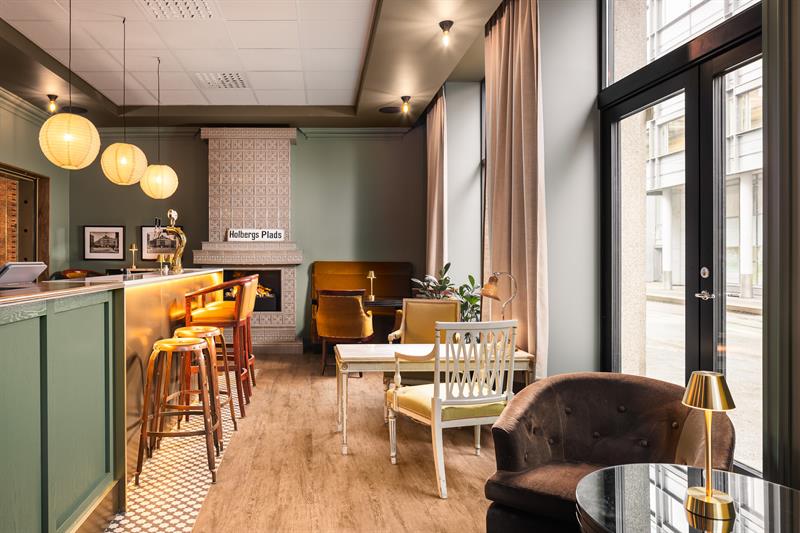 En lobbybar med peis, disk, lenestoler, bord og grønnmalte vegger.