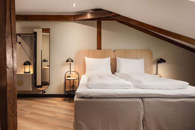 Et hotellrom med en dobbeltseng, et speil og en brun takbjelke som går langs taket.