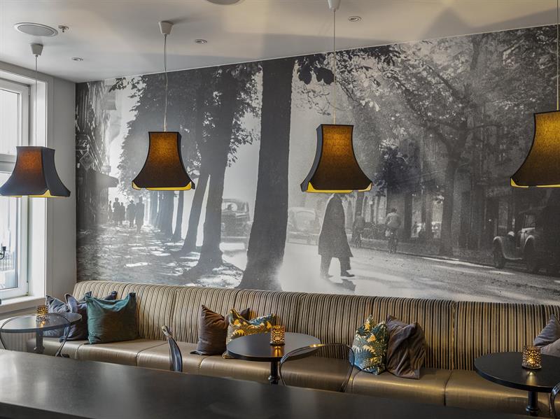 langsofa med puter. Fototapet med bymotiv. Brune lampetter over bordet. Saga Hotel Oslo. Foto