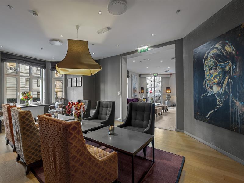 Sittegruppe med lenestoler i rødt og beige. Store vinduer. Tregulv. Kunst på Veggen. Saga Hotel Oslo. foto