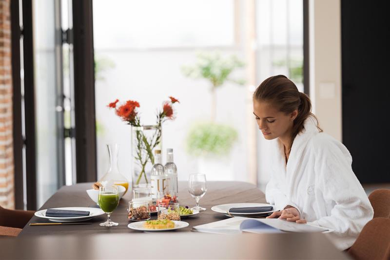 Dame spiser frokost og leser et magasin i hvit morgenkåpe