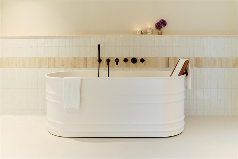 Badet har et frittstående badekar, veggmonterte armaturer og flislagte overflater. Designet for praktisk og komfortabel bruk.