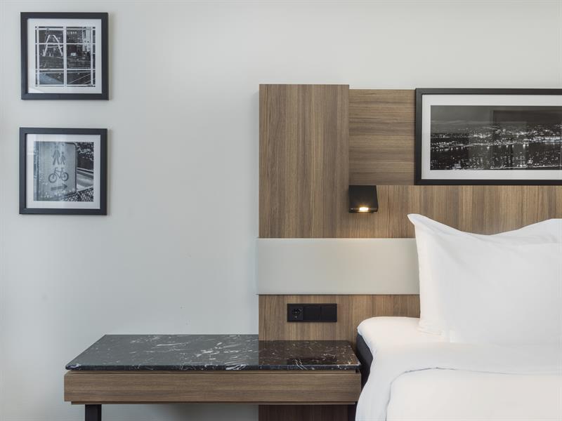 Detalj fra et hotellrom. Seng, nattbord, svart-hvitt-bilder i rammer. Foto