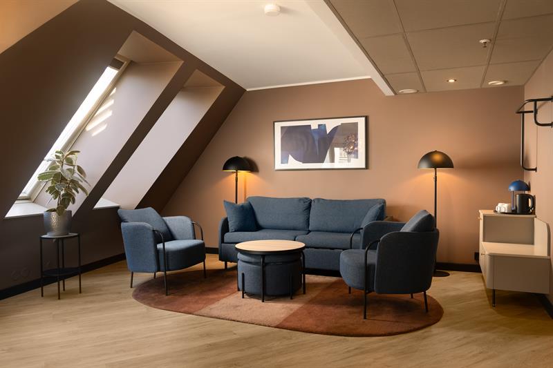 Hotellrom med blå sofa, blå lenestoler, beige vegger og store vinduer