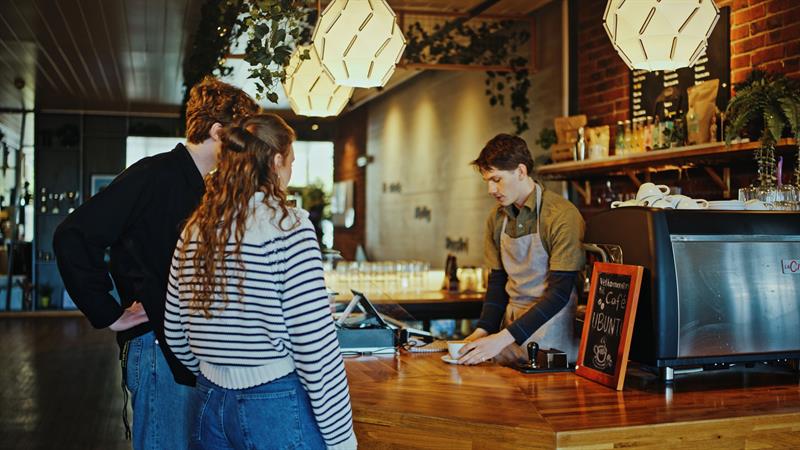 To kunder på en kafé med en barista bak disken