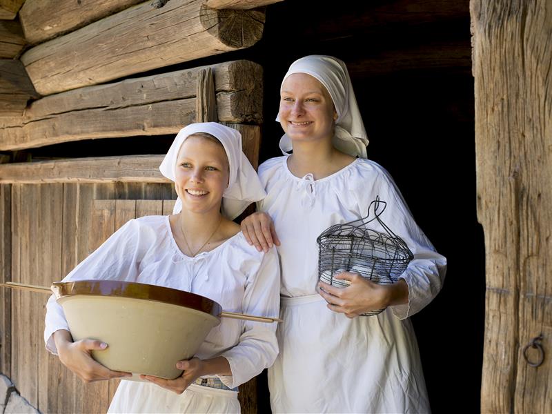 To unge kvinner foran en tradisjonell trebygning. Norsk Folkemuseum