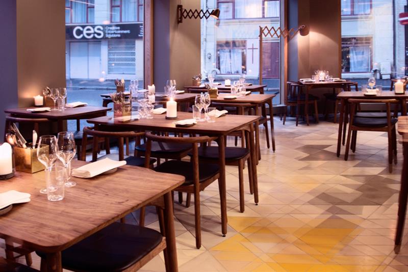 Restaurantinteriør med brune trebord og -stoler, med glass og servietter på dem. Skandinavisk interiørdesign.