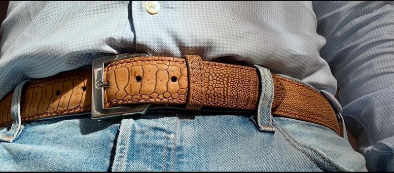 Et nærbilde av et brunt, strukturert skinnbelte som sitter rundt livet på en person i jeans.