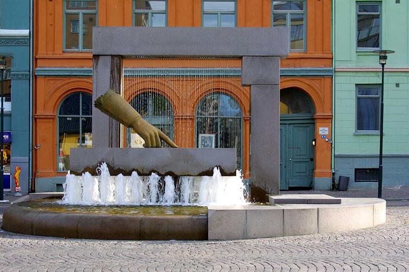 Byggets fasade bak en fontene med en statue av en hånd.