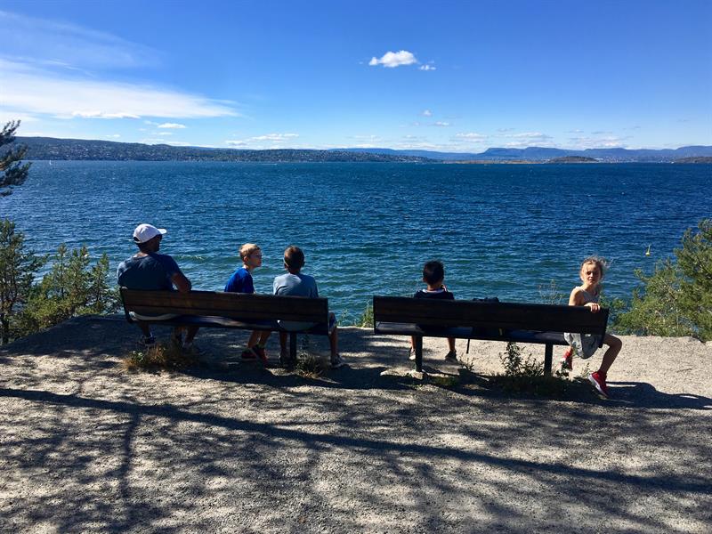 Folk som sitter på benker og ser ut over fjorden.