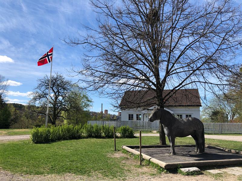 En hestestatue foran et hvitt trehus og en flaggstang.