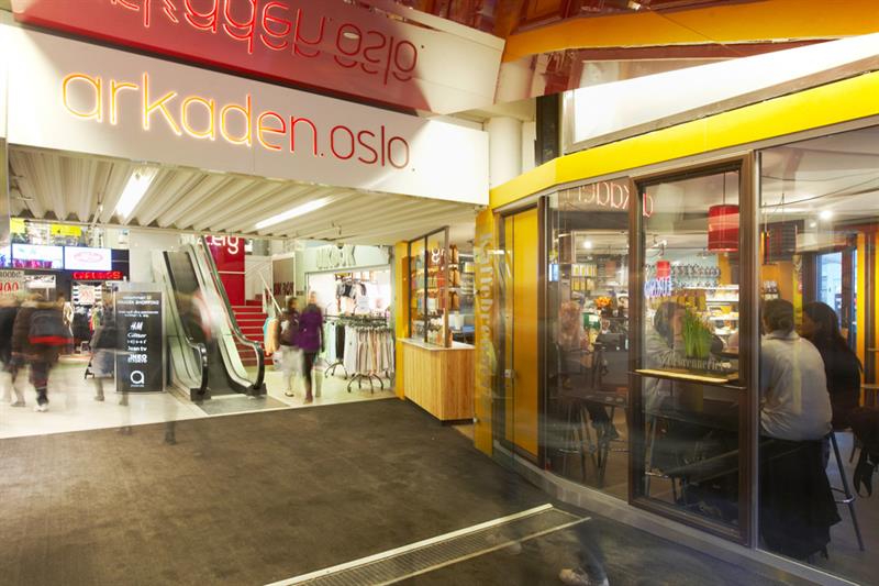 Interiør i kjøpesenteret. Utsiden av butikker, en rulletrapp og folk som går.