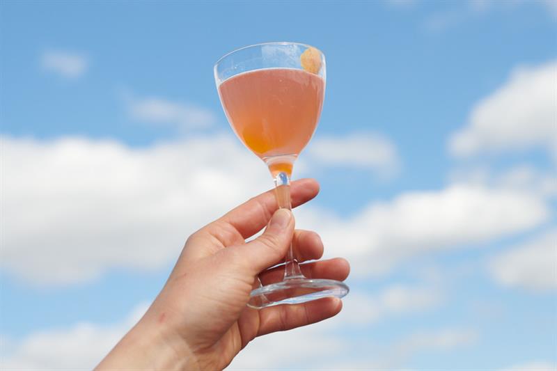 en person som holder et glass i luften, med blå himmel i bakgrunnen