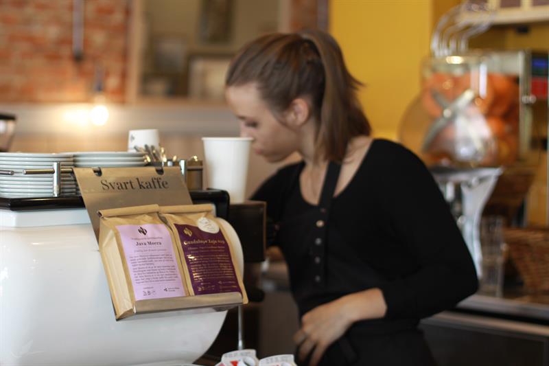Nærbilde av to utvalgte poser med kaffebønner, med en barista i bakgrunnen.