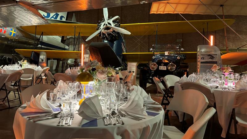 Runde bord er dekket til en gallamiddag i Luftfartshallen på Norges Vitenskaps- og Teknologimuseum, omgitt av historiske fly og veteranbiler