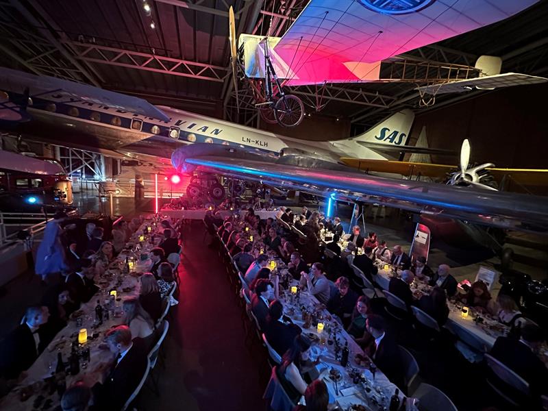 Lange bankettbord dekket til middag under klassiske fly i Aviation Hall, opplyst av stemningsfull belysning.