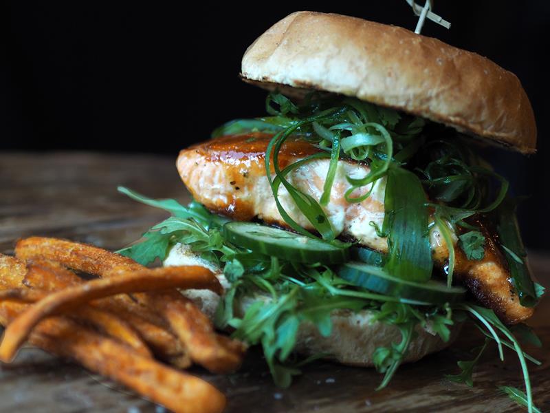 Detaljbilde av en burger og litt pommes frites som ligger spredt rundt.