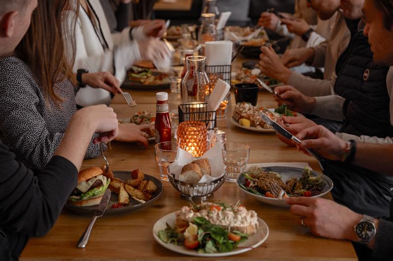 Gjestene samlet seg rundt et langt bord og nøt mat og drikke i en varm og hyggelig restaurantatmosfære.