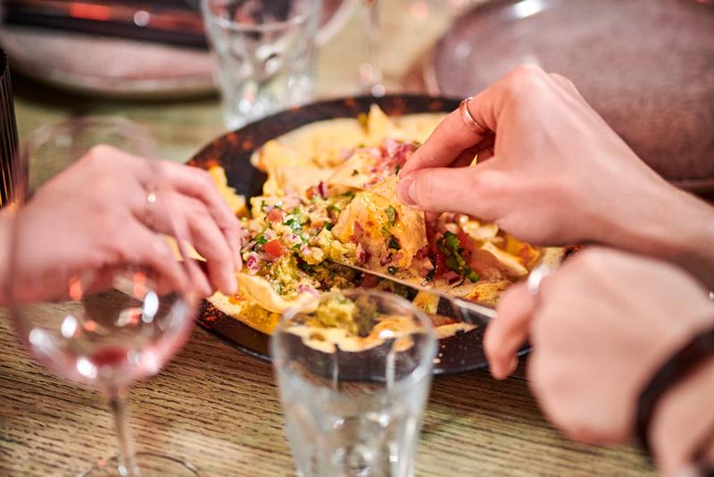 Folk som deler en tallerken med nachos ved et bord med vin- og vannglass.