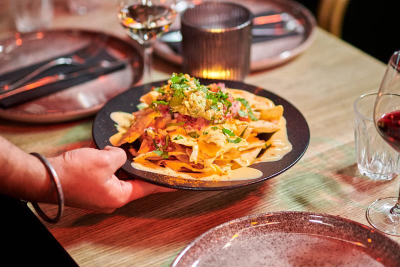 En tallerken med nachos som serveres ved et bord dekket med glass og bestikk.