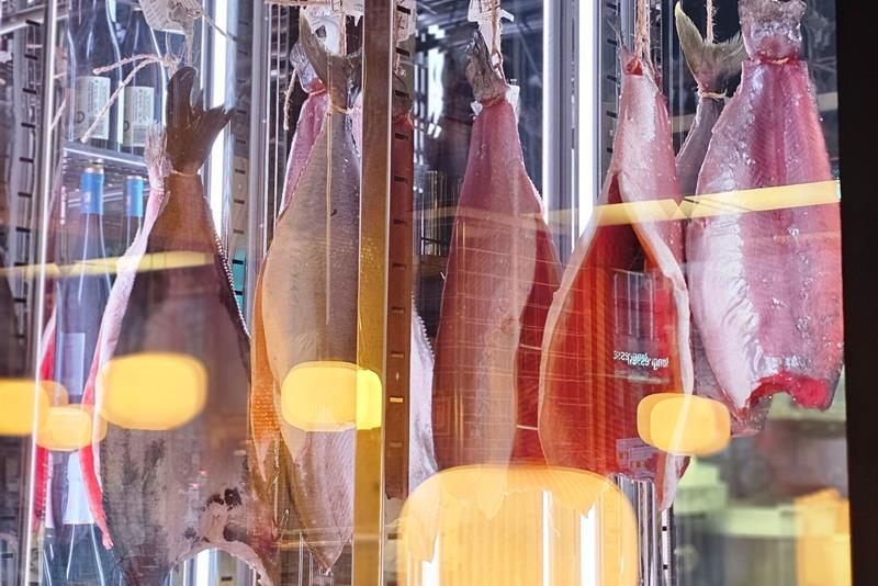 Store fiskefileter henger til modning inne i et kjølt glasskap