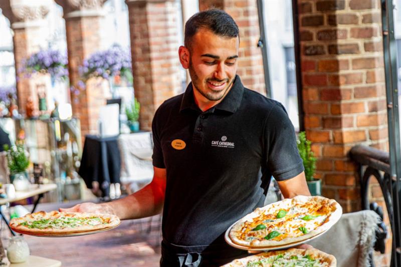 En servitør som bærer tre pizzaer.