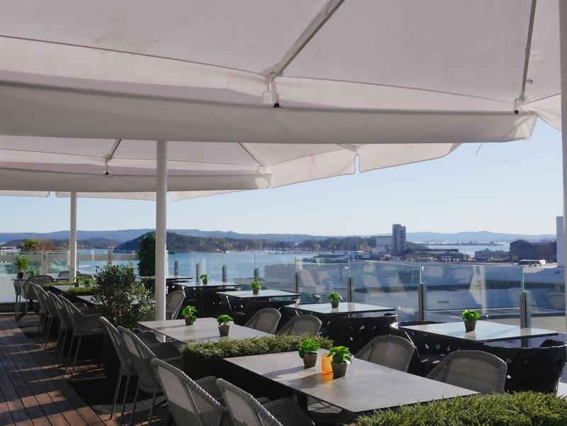 Stilig takterrasse med bord, glassrekkverk og utsikt mot fjorden.