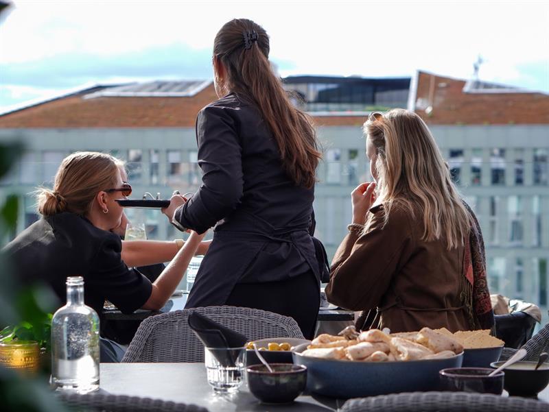 Gjester som nyter mat og drikke på en solfylt takterrasse i Oslo.