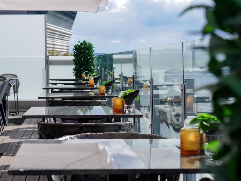 Stilig takterrasse med bord, glassrekkverk og utsikt mot fjorden.