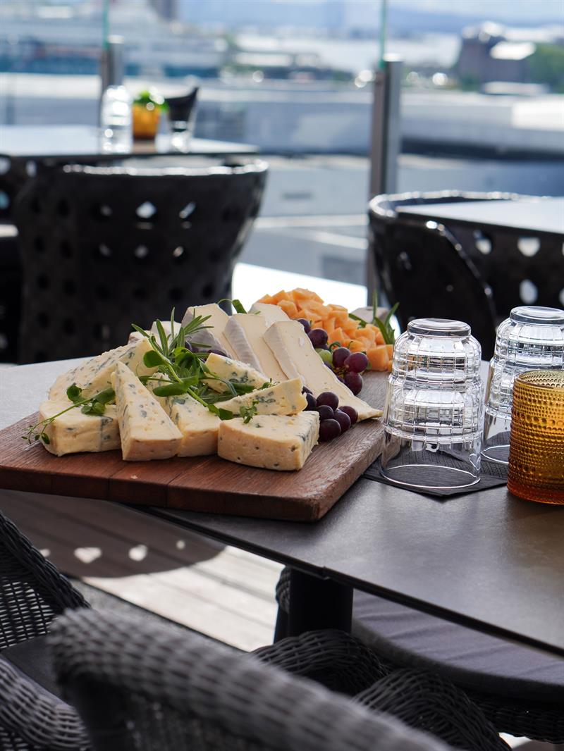 Ostefat og småretter serveres på en takterrasse med utsikt over byen.