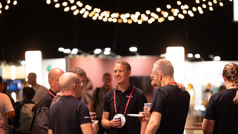 Flere personer med navneskilt står sammen og snakker på en konferanse eller et nettverksarrangement.