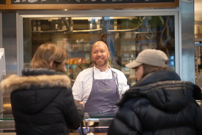 En ansatt bak disken hjelper to kunder