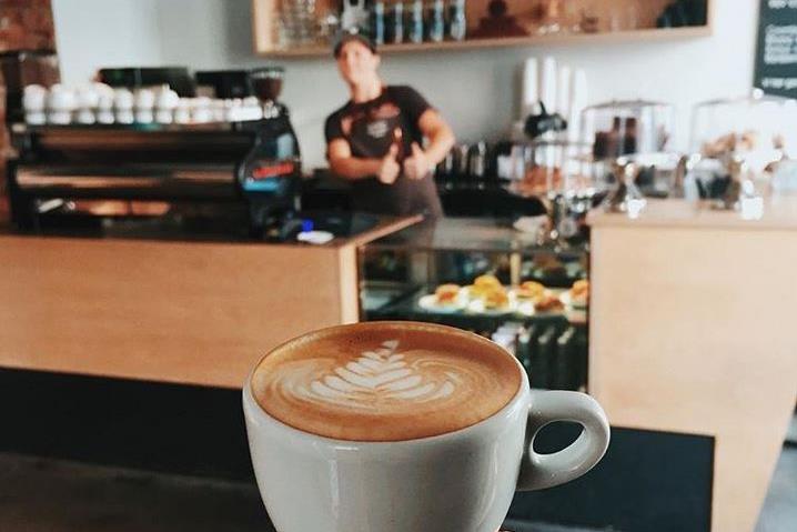 en hånd som holder opp en kaffe med kaffebaren i bakgrunnen