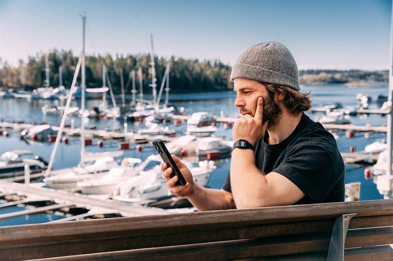 En mann som sitter med mobiltelefonen sin ved en havn