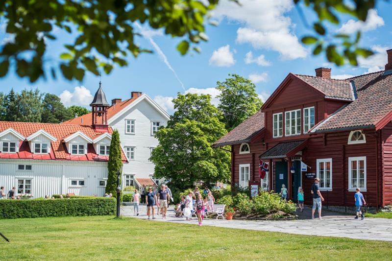 En solrik dag med trehus, plen og folk som går tur.