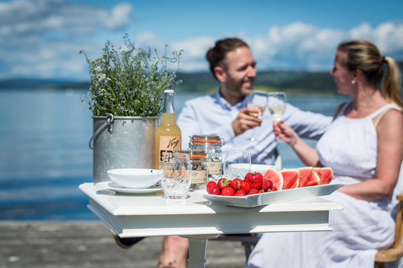 To personer som sitter og skåler ved et bord med jordbær og vannmelonbiter på.