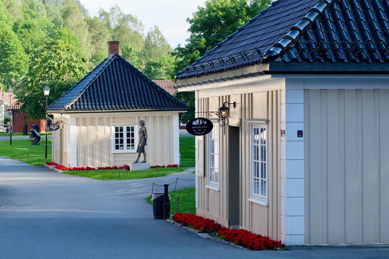 To lave trehus, en statue mellom dem, røde blomster i blomsterbedene.