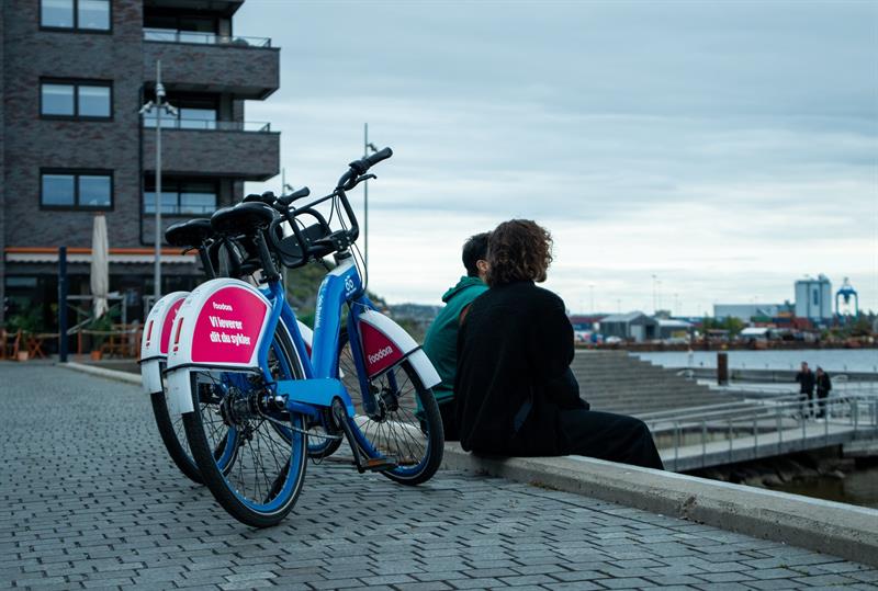 To personer som sitter på kanten av en brygge, med to bysykler bak seg.