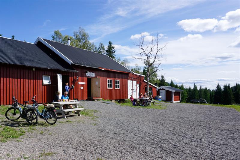 Et rødt hus ved skogen, med et par mennesker som sitter utenfor.