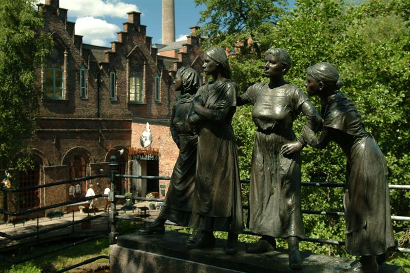 Statue of four girls with trees and a building in the background.