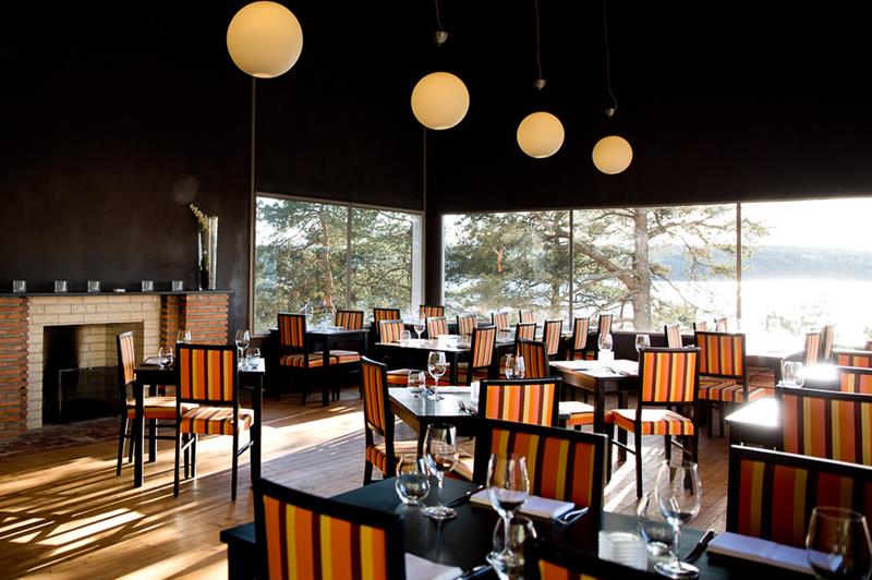 Black tables and striped chairs, a fireplace and large panoramic windows with a good view.