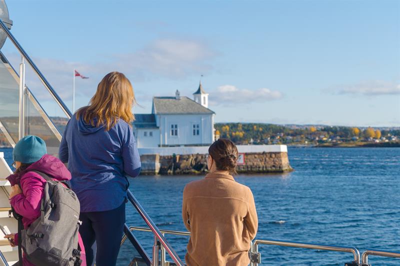 People looking at a lighthouse in the fjord from the boat