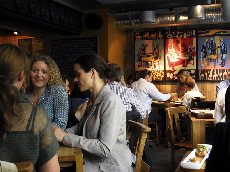 Restaurantinteriør med mennesker som spiser og snakker sammen.