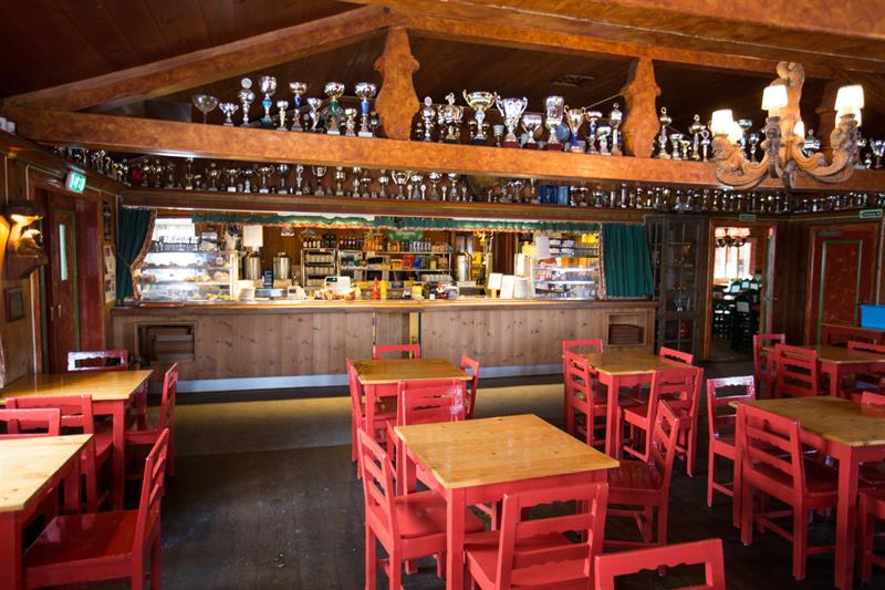 A café interior with a lofted ceiling, small red tables and chairs, and many trophies displayed on the ceiling beams.
