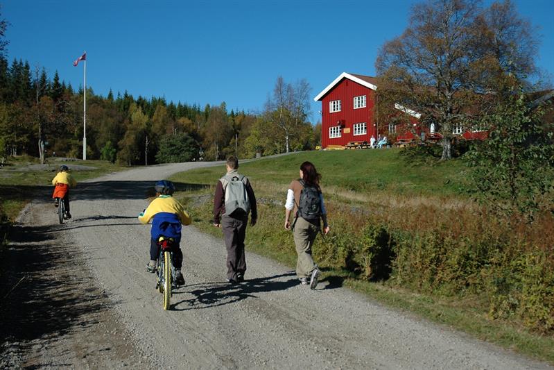 People walking and cycling towards a red cabin in the woods.