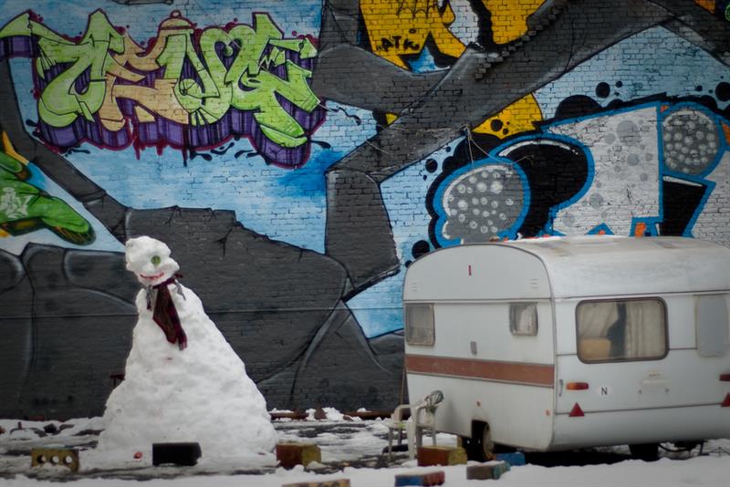 En snømann og en campingvogn foran en vegg med graffiti.