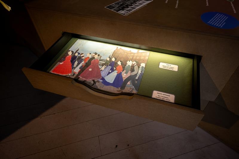 Interaktiv museumsinstallasjon med en opplyst skuff som viser illustrasjoner og tekstbaserte aktiviteter.