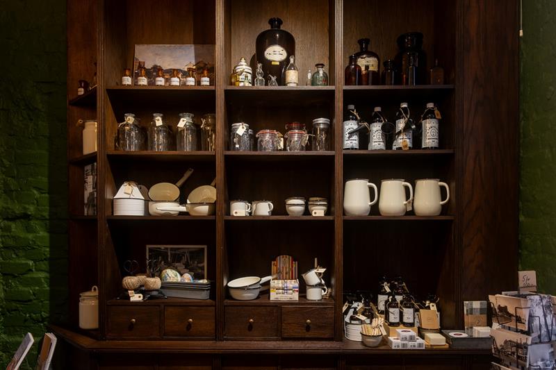 Museumsutstilling med hyller fylt med glasskrukker, emaljevarer og historiske husholdningsartikler.