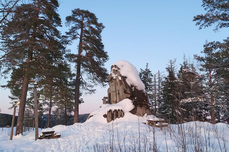 Trollstatue dekket av snø, omgitt av trær